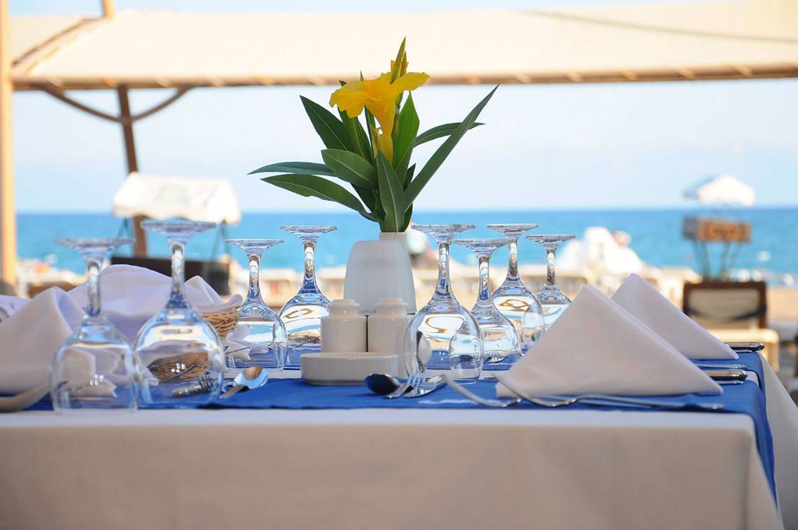 Gedeckter Tisch am Strand mit Blumen in einer Vase und Blick auf das Meer.