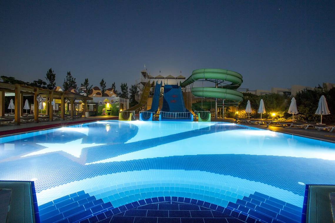 Nachtansicht des Swimmingpools im Fame Residence Lara & Spa Hotel mit Wasserrutschen und Sternendesign.
