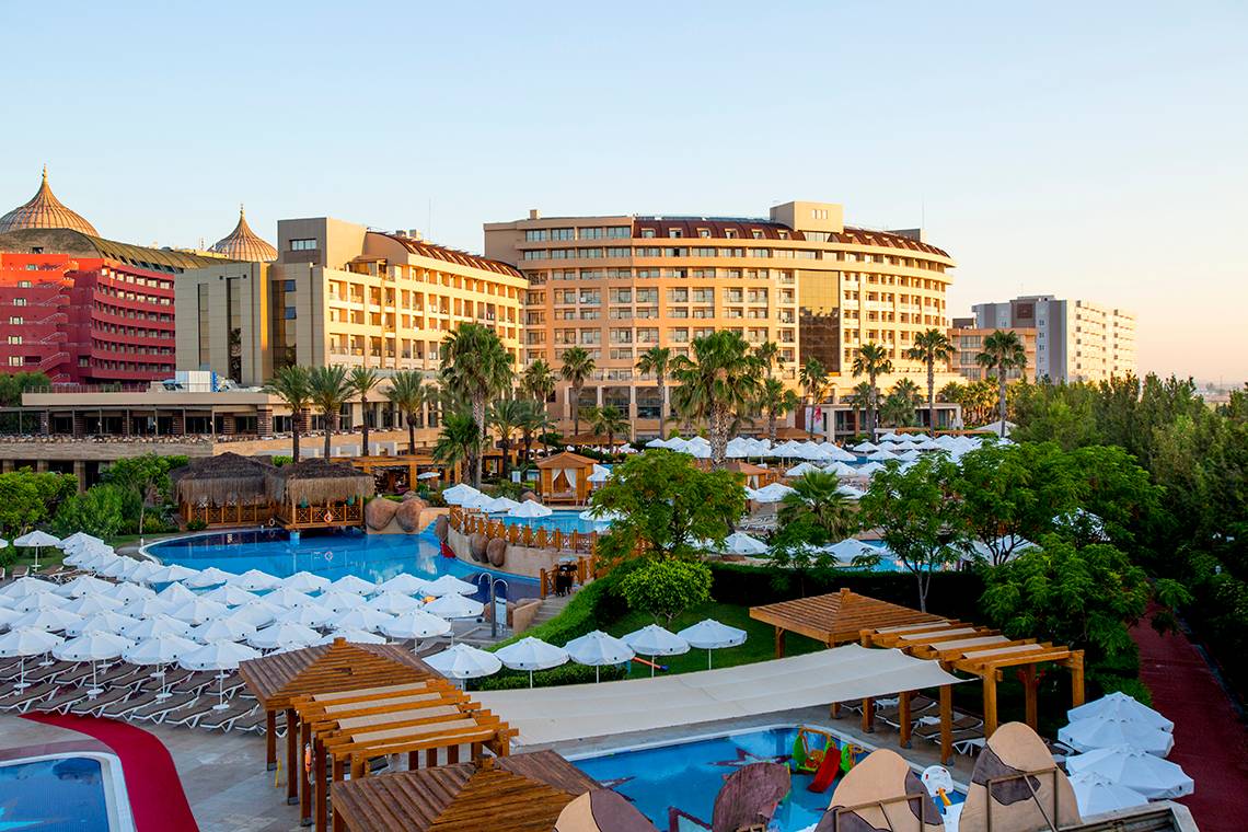 Außenansicht des Fame Residence Lara & Spa Hotels mit Swimmingpools, Sonnenschirmen und Gebäuden im Hintergrund.