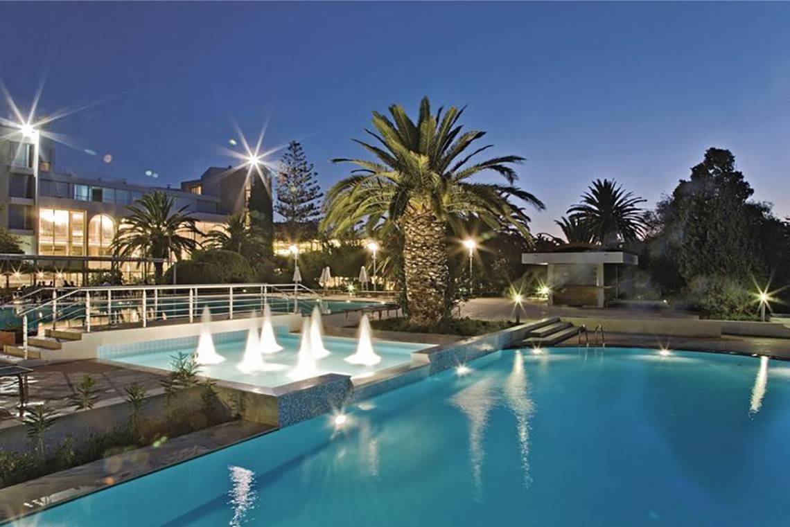 Der Pool des Caravia Beach Hotel bei Nacht mit Springbrunnen und Beleuchtung.