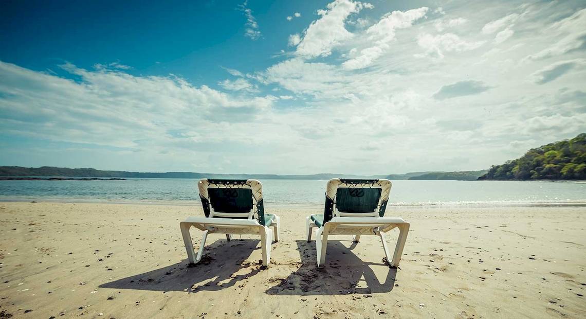 Zwei Sonnenliegen stehen am Strand des Occidental Papagayo Hotels mit Blick auf das Meer.