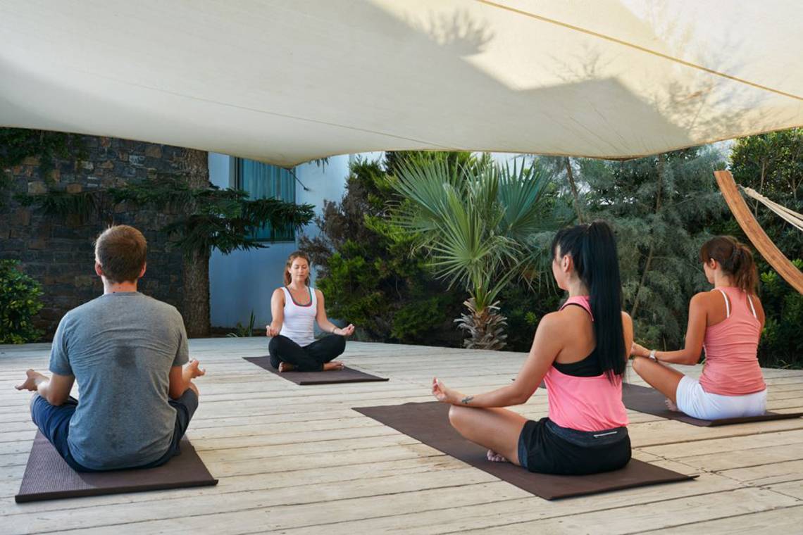 Vier Personen, die einen Yogakurs im Freien auf dem Island Hotel in Kreta absolvieren.