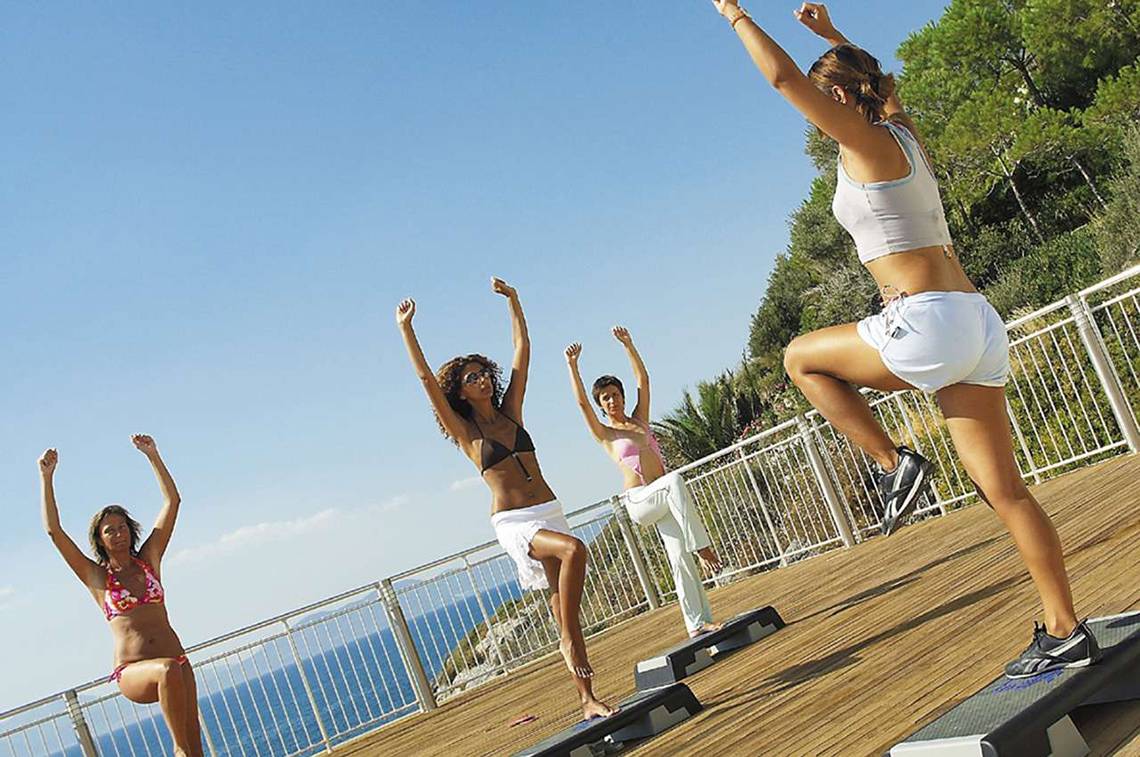 Vier Frauen machen Workout auf einer Terrasse mit Blick auf das Meer.
