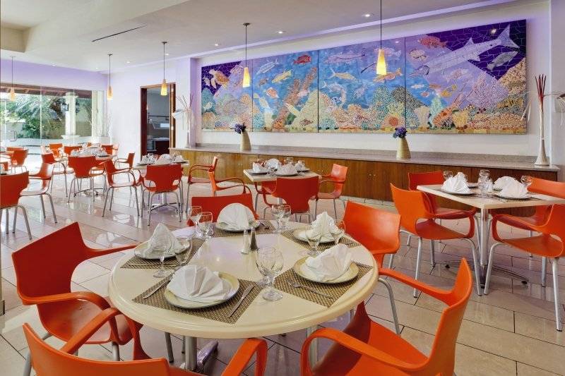 Innenansicht des Restaurants im Holiday Inn Resort Aruba mit orangen Stühlen und Tischen, einer großen Wandmalerei und einer Theke.