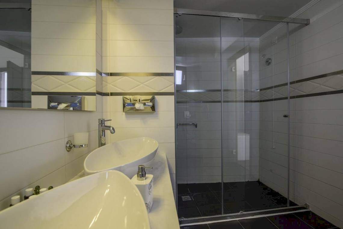Badezimmer des La Mer Deluxe Hotel & Spa mit zwei Waschbecken, Glasdusche und Spiegel.