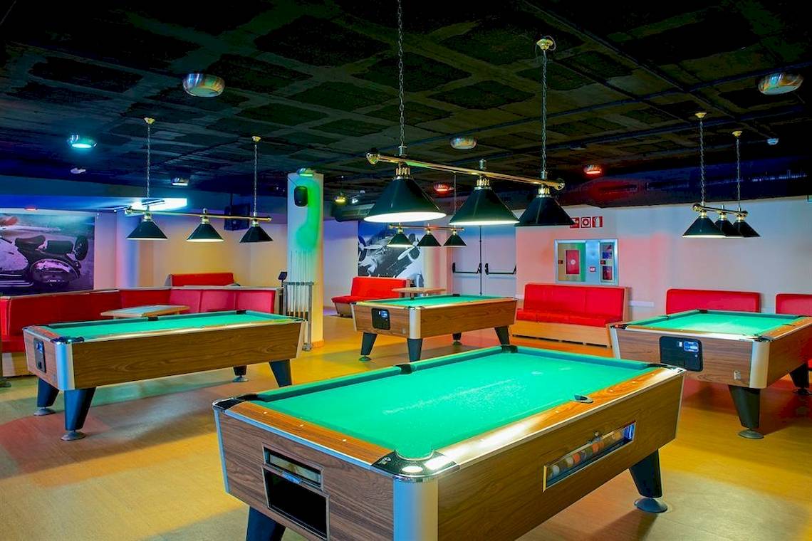 Billardhalle mit mehreren grünen Billardtischen und roten Sofas