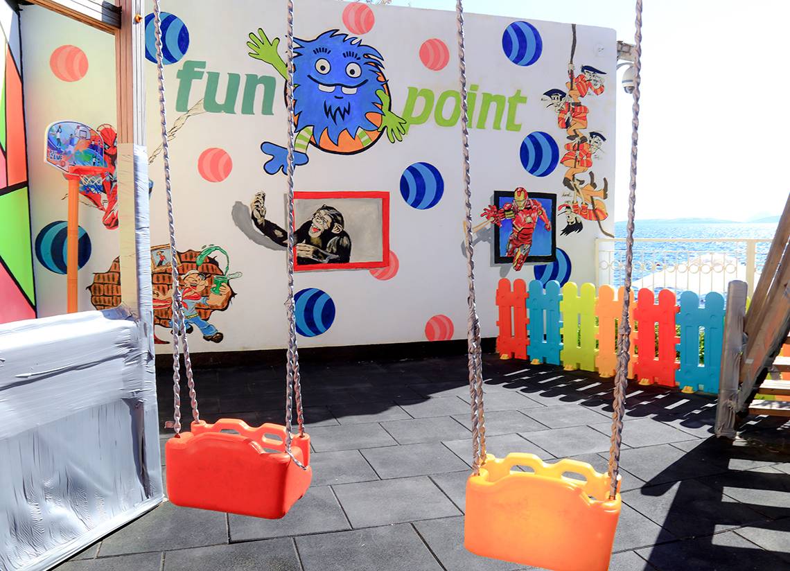 Spielplatz im LABRANDA TMT Bodrum Hotel mit bunten Schaukeln und einer Wandmalerei von einem Affen und einem Piraten.