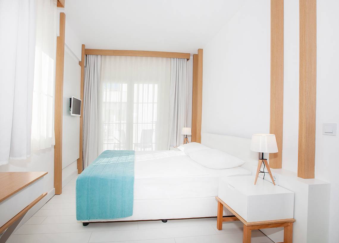 Schlafzimmer im LABRANDA TMT Bodrum Hotel mit weißem Bett, blauer Decke, zwei Lampen und weißem Nachttisch.