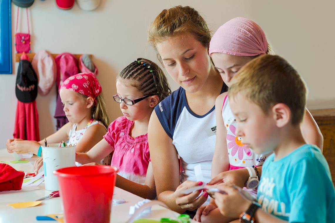 Gruppe von Kindern und einer Erzieherin basteln in einem Hotelzimmer