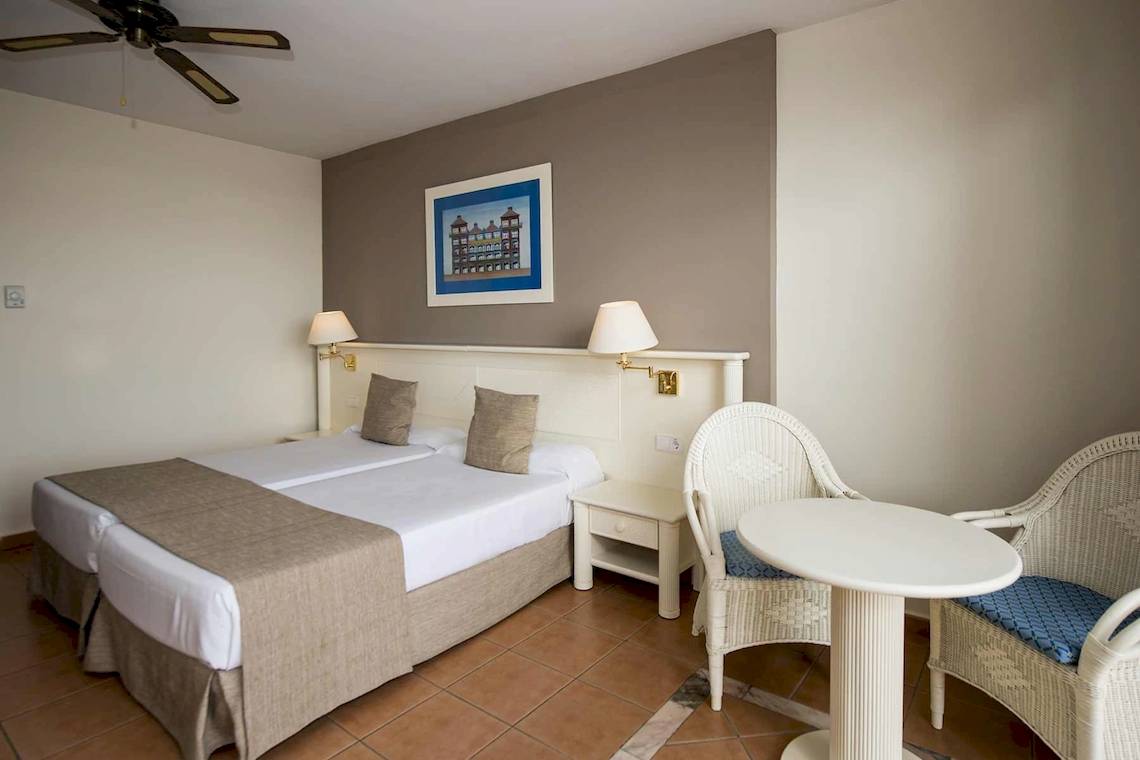 Doppelbett-Zimmer im Bahia Principe Sunlight Costa Adeje Hotel mit Nachttischen, Stühlen und Gemälde.