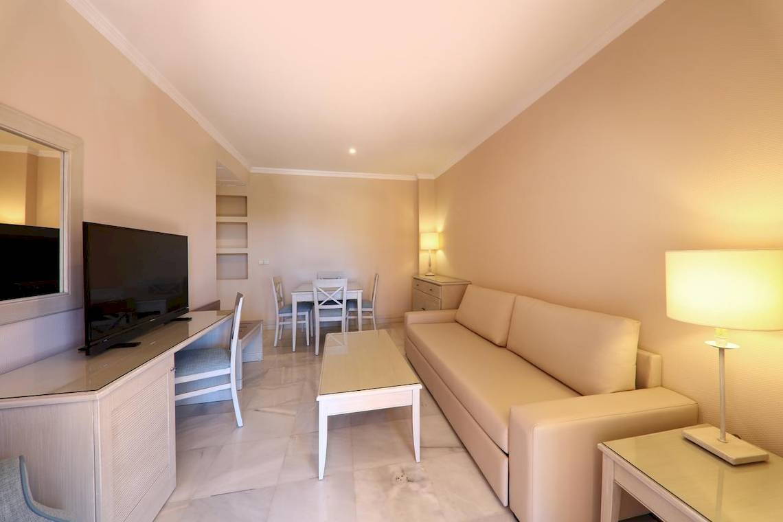 Wohnbereich im Iberostar Malaga Playa Hotel mit Sofa, Fernseher, Tisch und Lampe.