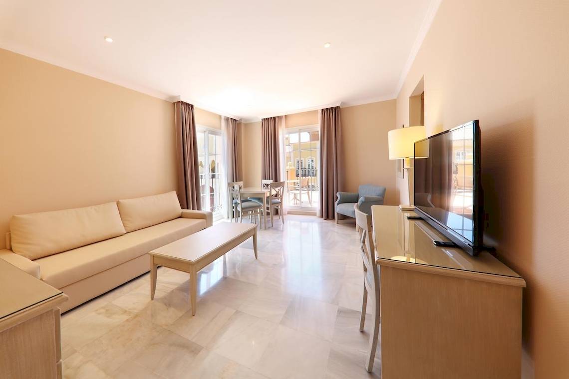 Innenansicht eines Hotelzimmers im Iberostar Malaga Playa mit Wohnzimmer, Couch, Tisch, Fernseher und Esstisch.