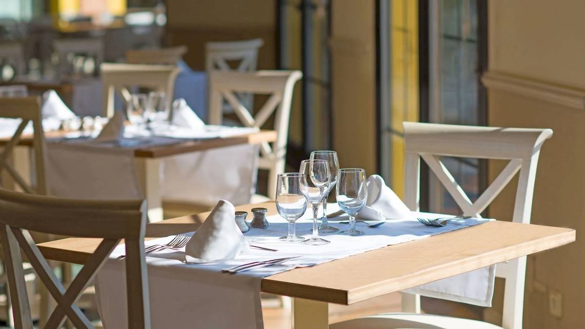 Ein gedeckter Tisch in einem hellen Restaurant mit Wein- und Wassergläsern, Besteck und Servietten.