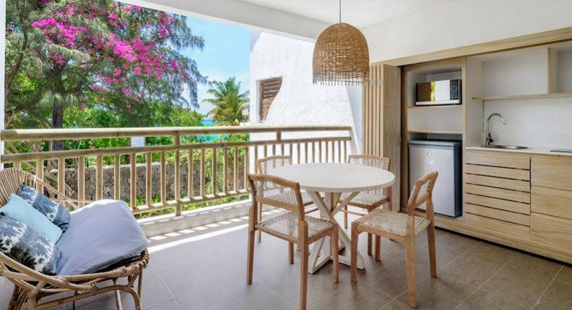 Balkon des Recif Attitude Hotels mit Tisch, Stühlen, Kissen und Küchenzeile.
