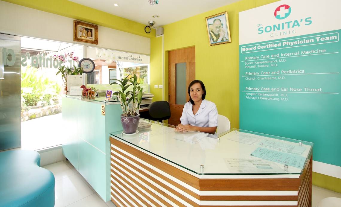 Frau an der Rezeption von Dr. Sonitas Clinic, in weißem Arztkittel, sitzt am Schreibtisch
