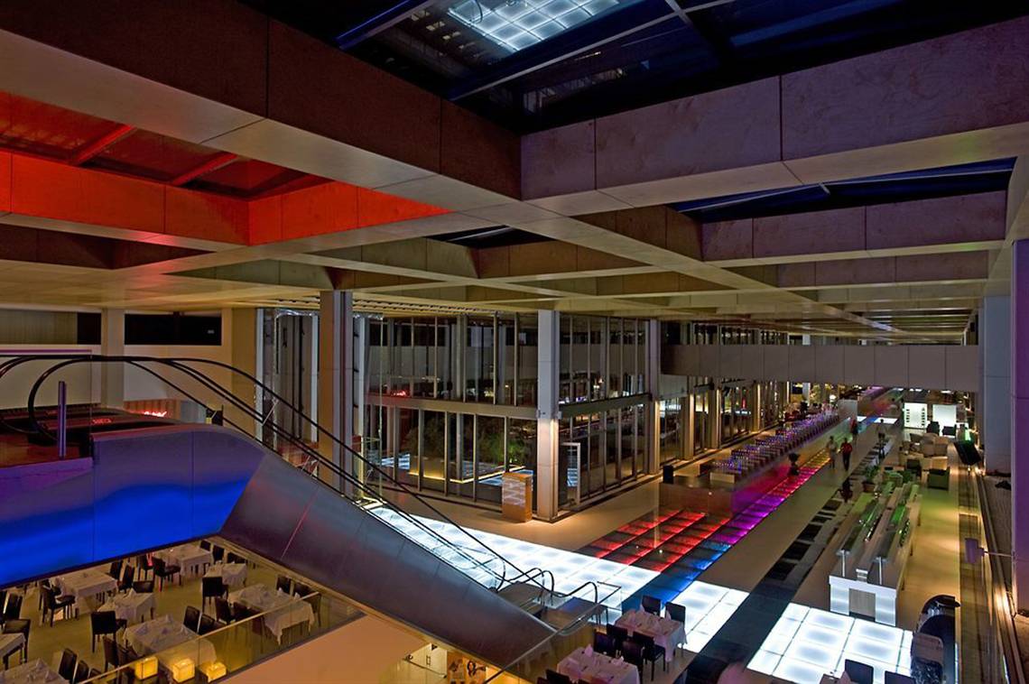 Innenansicht des Nirvana Cosmopolitan Hotels mit Lobby, Essbereichen und bunt beleuchteten Wegen.