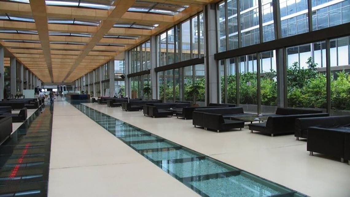 Lobby des Nirvana Cosmopolitan Hotels mit langen Glasflur und schwarzen Sofas.