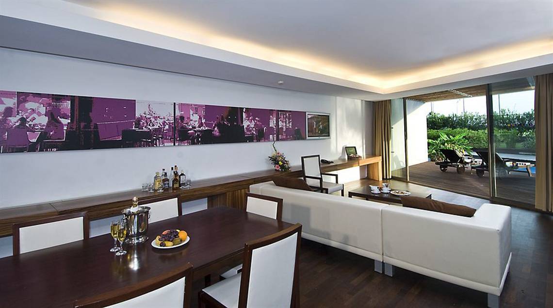 Loungebereich im Nirvana Cosmopolitan Hotel mit weißen Möbeln, einer großen Couch, Esstisch und Glaswänden.