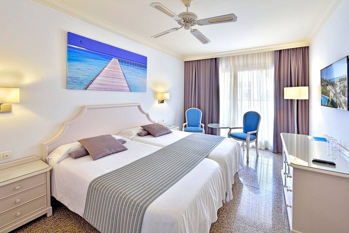 Hotelzimmer im MAC Puerto Marina mit zwei Betten, blauen Stühlen, Deckenventilator und Flachbildfernseher.