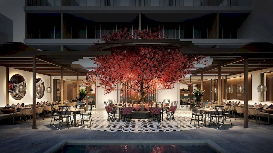 Innenbereich des Ikos Andalusia Hotels mit zentralem rot blühendem Baum, Tischen und Stühlen um das Atrium.