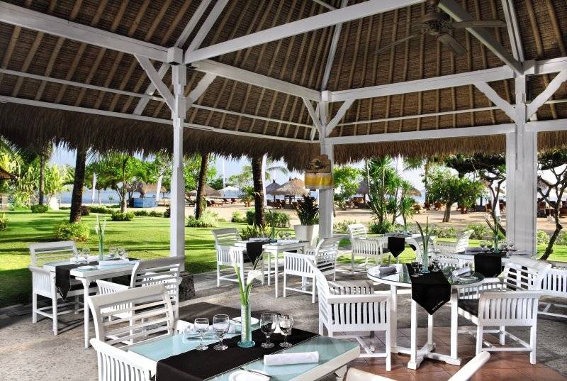 Außenbereich des Sol Benoa Bali Restaurants mit weißen Tischen und Stühlen unter einem Strohdach.