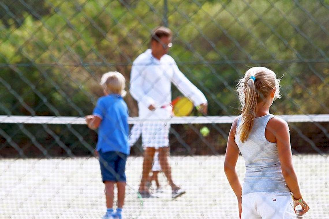 Tennisspieler auf einem Tennisplatz, ein Mann mit Schläger, zwei Kinder beobachten.