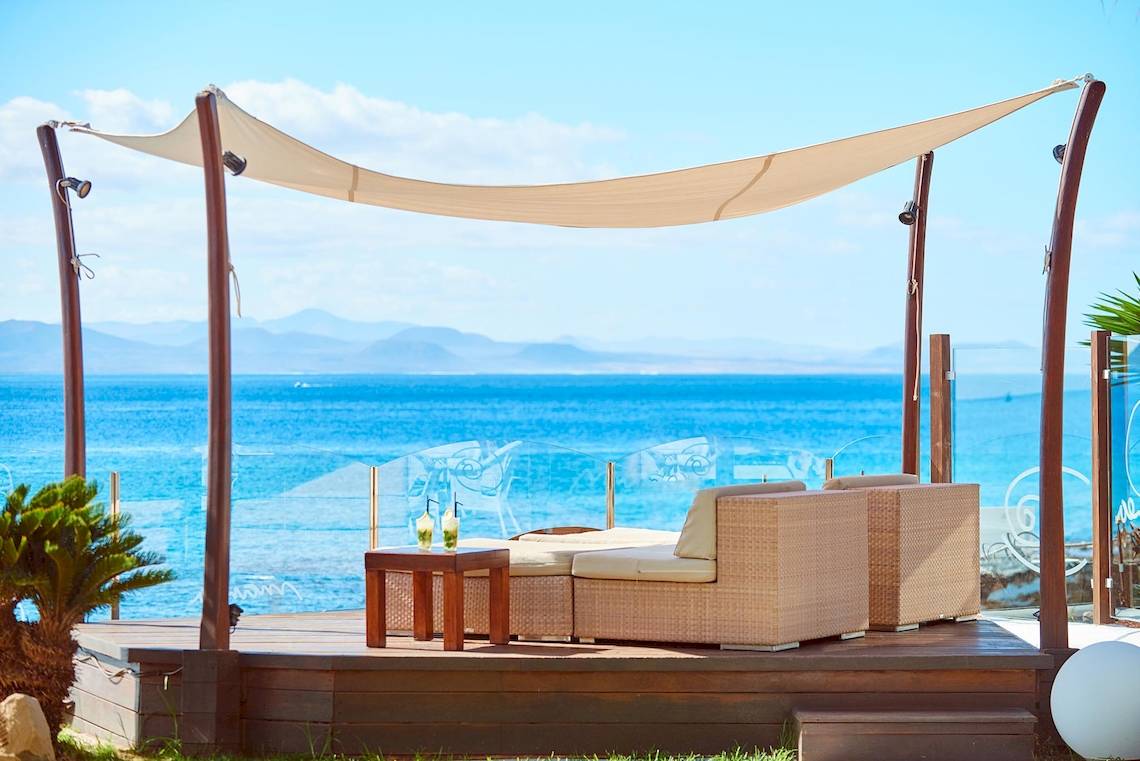 Lounge-Bereich im Hipotels Natura Palace mit Blick auf das Meer und einer beschatteten Sitzgelegenheit.