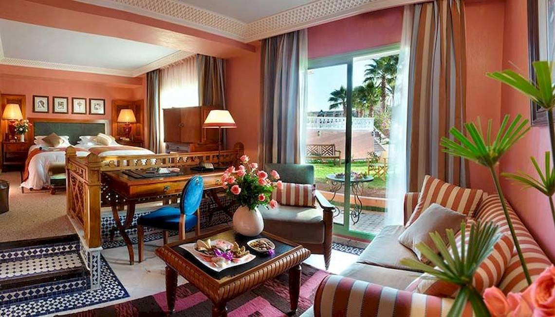 Innenansicht eines Zimmers im Palmeraie Palace Hotel mit Bett, Schreibtisch, Sofa und Gartenblick.