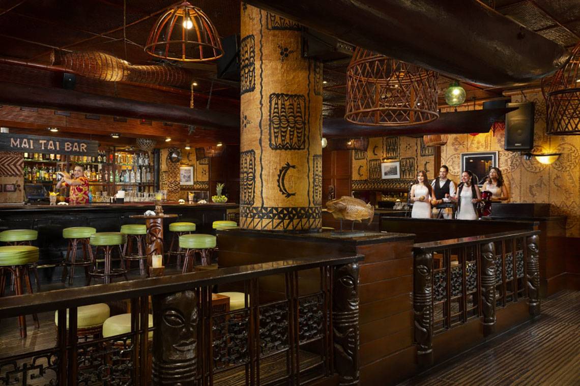 Innenansicht der Bar im Beach Rotana Hotel mit grünen Stühlen und einer Gruppe von Leuten am Tresen.