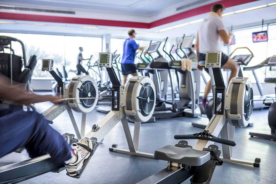 Fitnessstudio mit Rudergeräten und Laufbändern, mehrere Personen trainieren