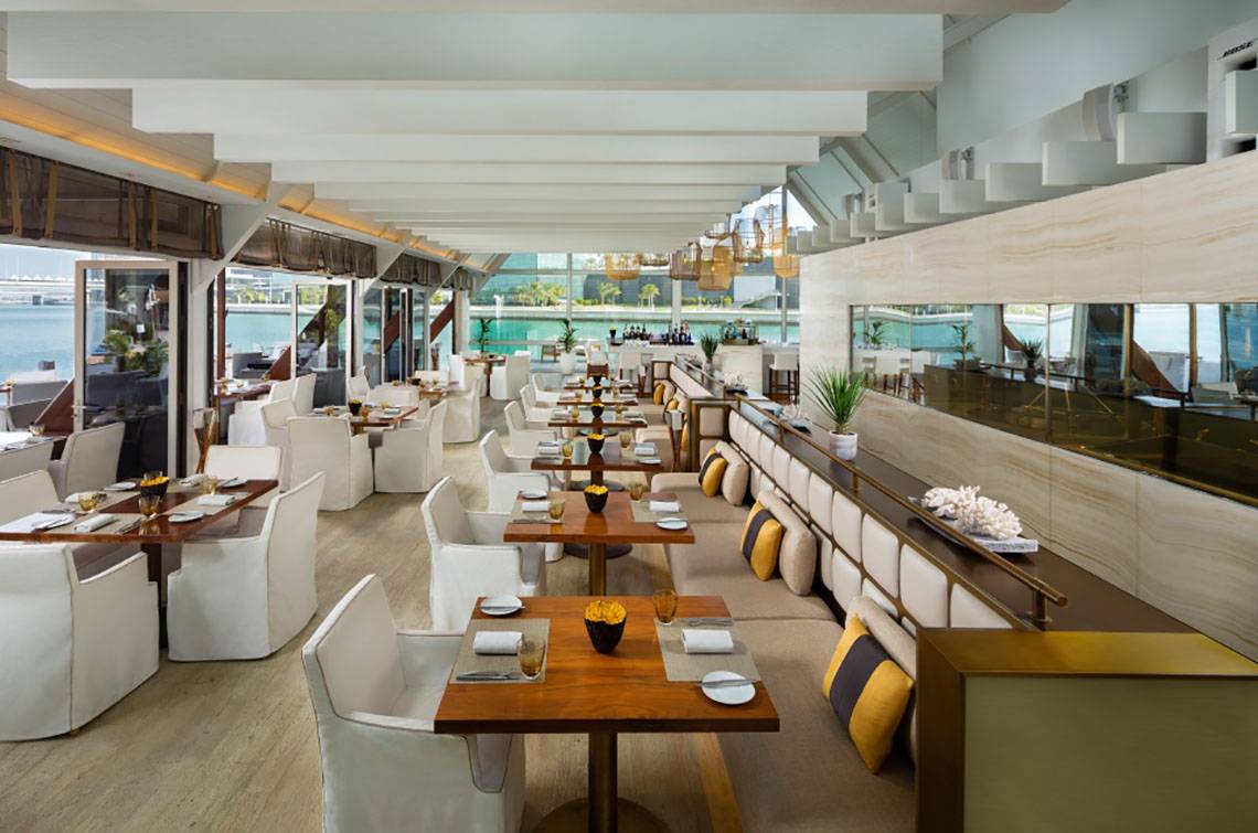 Innenansicht des Restaurants im Beach Rotana mit weißen Tischen und Stühlen und Blick auf das Meer.
