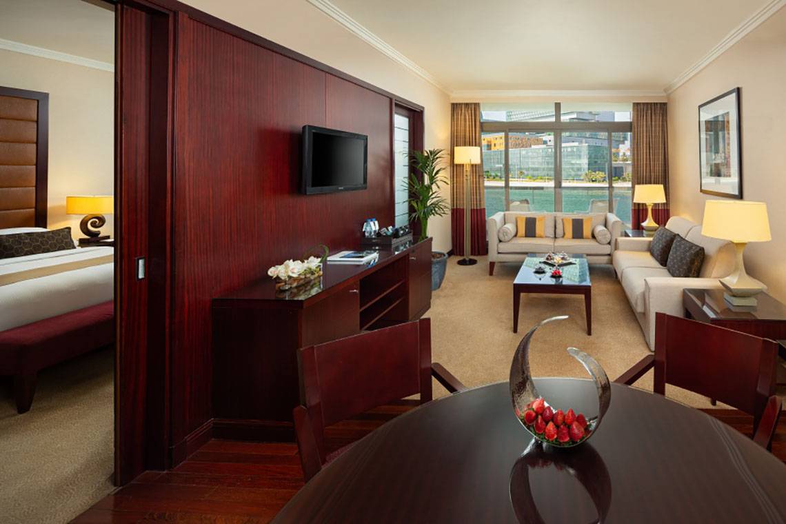 Innenansicht einer Suite im Beach Rotana Hotel mit Wohnzimmer, Schlafzimmer und Schreibtischbereich.
