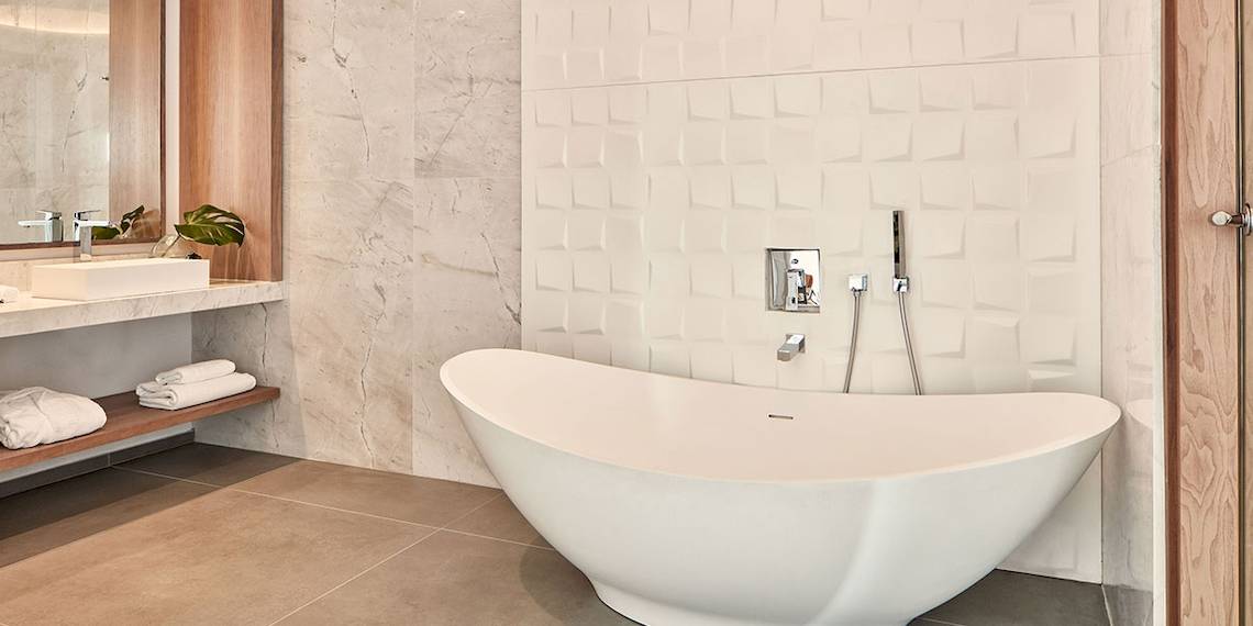 Ein Badezimmer mit einer freistehenden weißen Badewanne und gemusterten weißen Fliesen an der Wand.