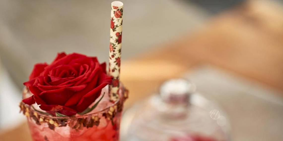 Ein roter Cocktail in einem Glas mit einer roten Rose auf einem Strohhalm