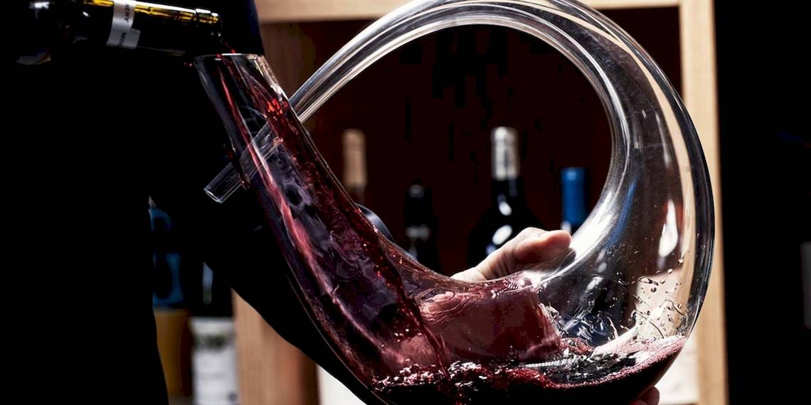 Person gießt Wein aus einer Flasche in ein geschwungenes Glas