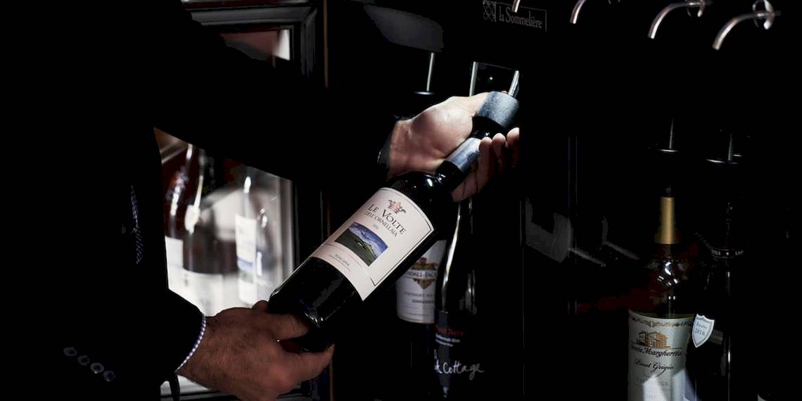 Ein Mann entkorkt eine Flasche Wein im Hotel Myconian Korali Relais & Chateaux.