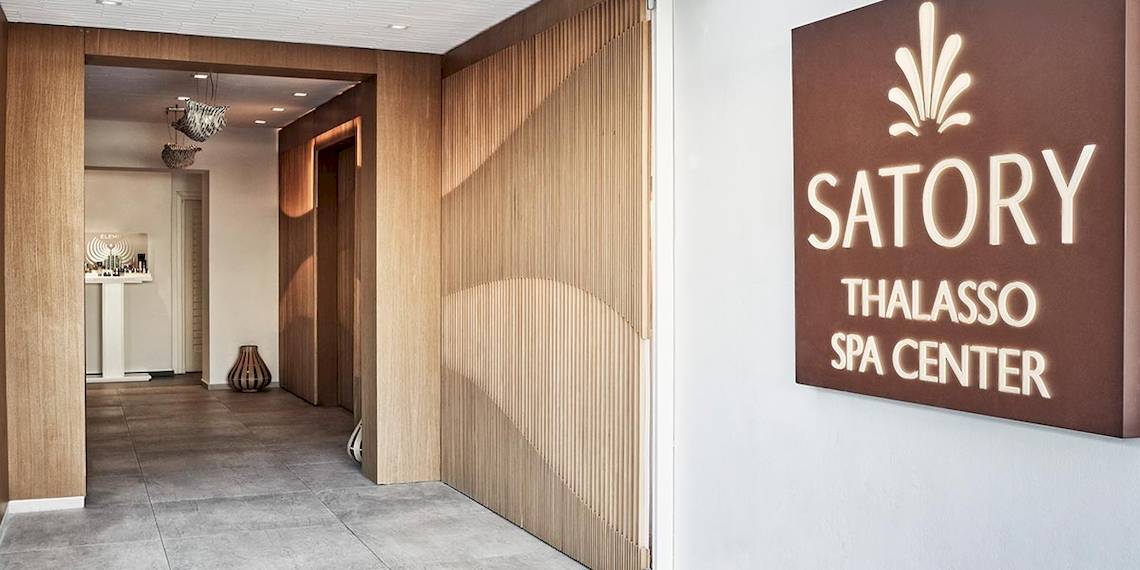 Eingang des Satory Thalasso Spa Center mit geometrischen Holzwänden und einem Schild, das den Namen des Spas anzeigt.