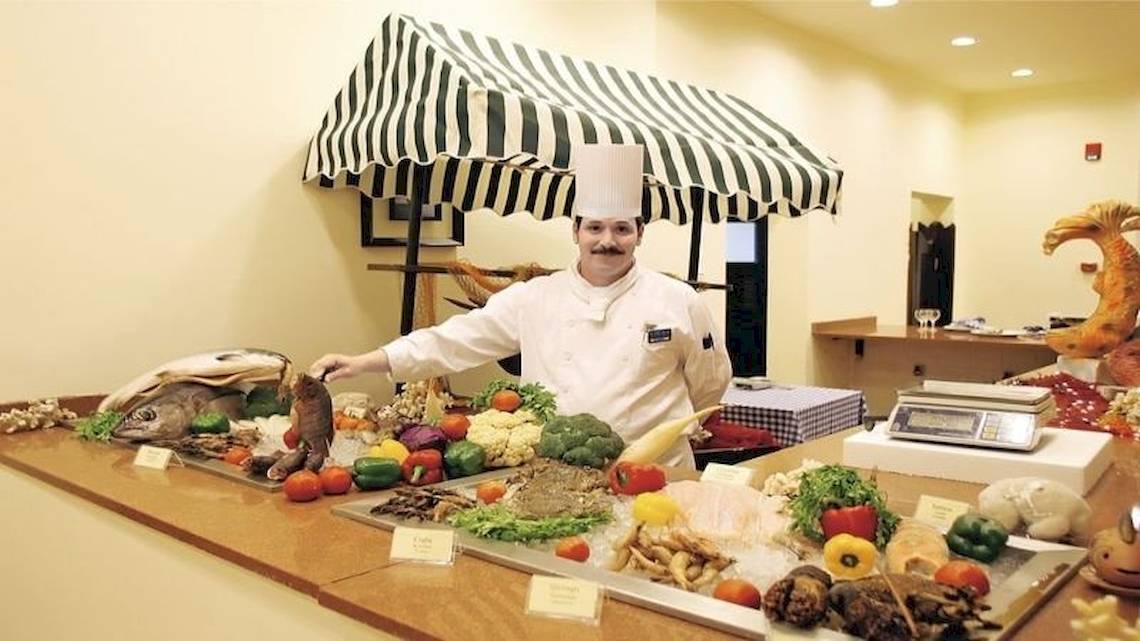 Koch im Restaurant des Serenity Alpha Beach Hotels mit einer Auswahl an frischen Lebensmitteln.