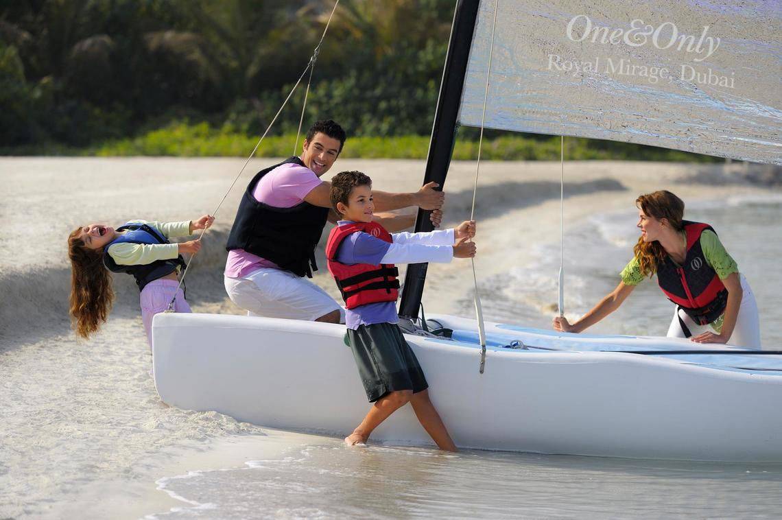 Eine Familie zieht ein Segelboot am Strand mit dem Hotelnamen The Palace At One & Only Royal Mirage, Dubai.