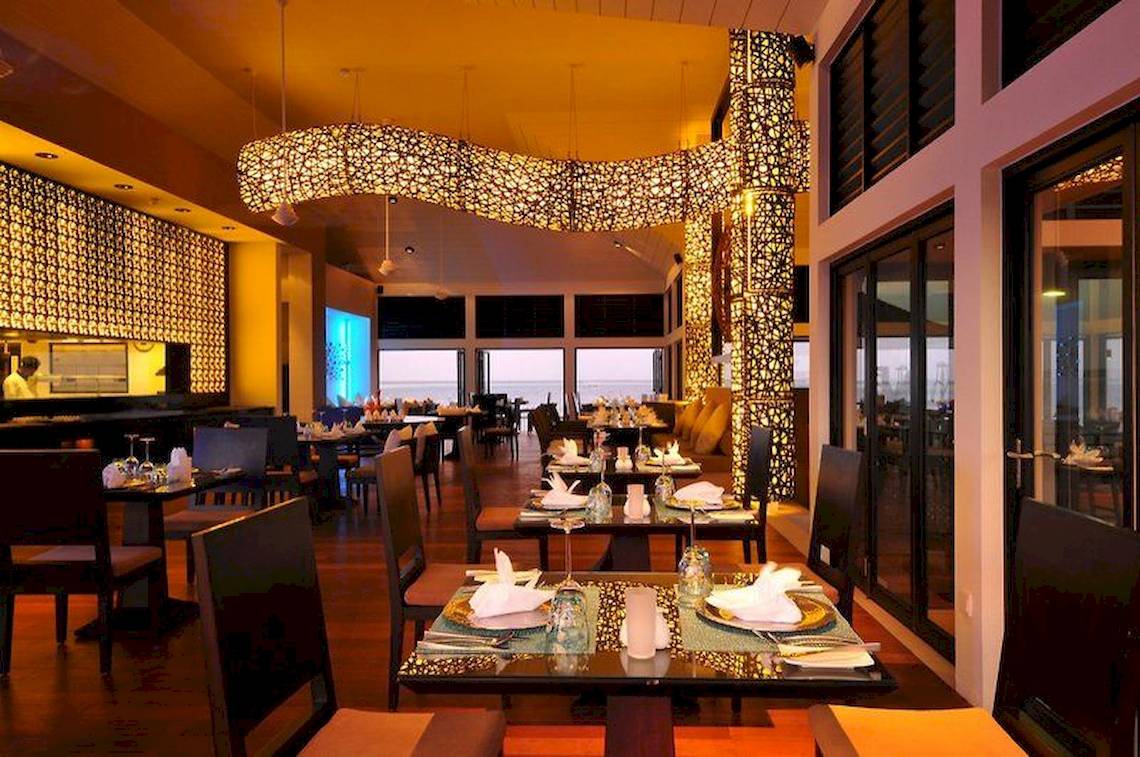 Innenansicht des Restaurants im Angsana Velavaru Hotel mit gedeckten Tischen und dekorativen Wandleuchten.