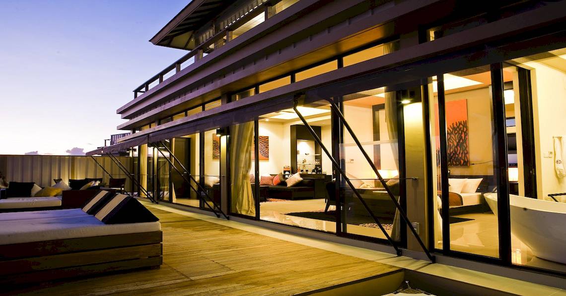Außenbereich des Angsana Velavaru Hotels mit Terrasse, Loungebereich und großen Glasfenstern.