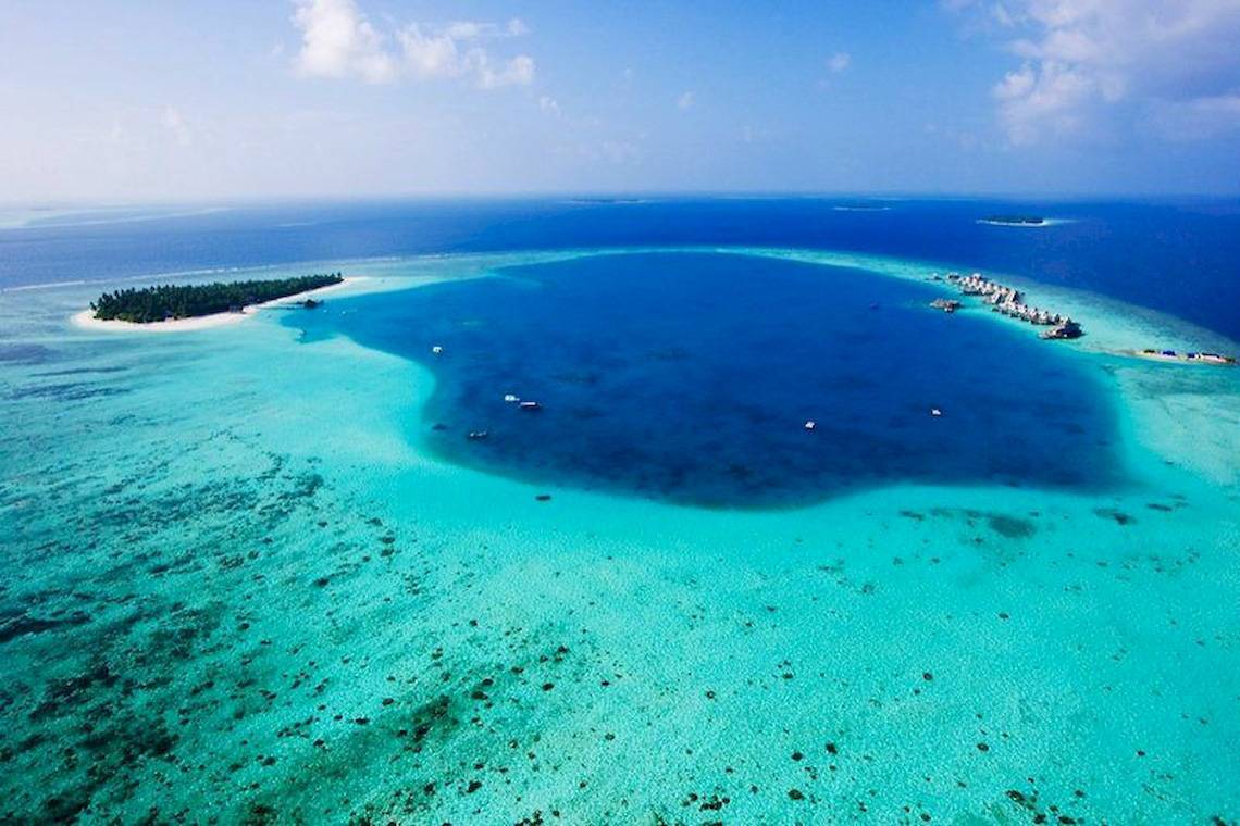 Luftaufnahme des Angsana Velavaru Resorts auf einer Insel mit türkisfarbenem Wasser und weißen Sand.