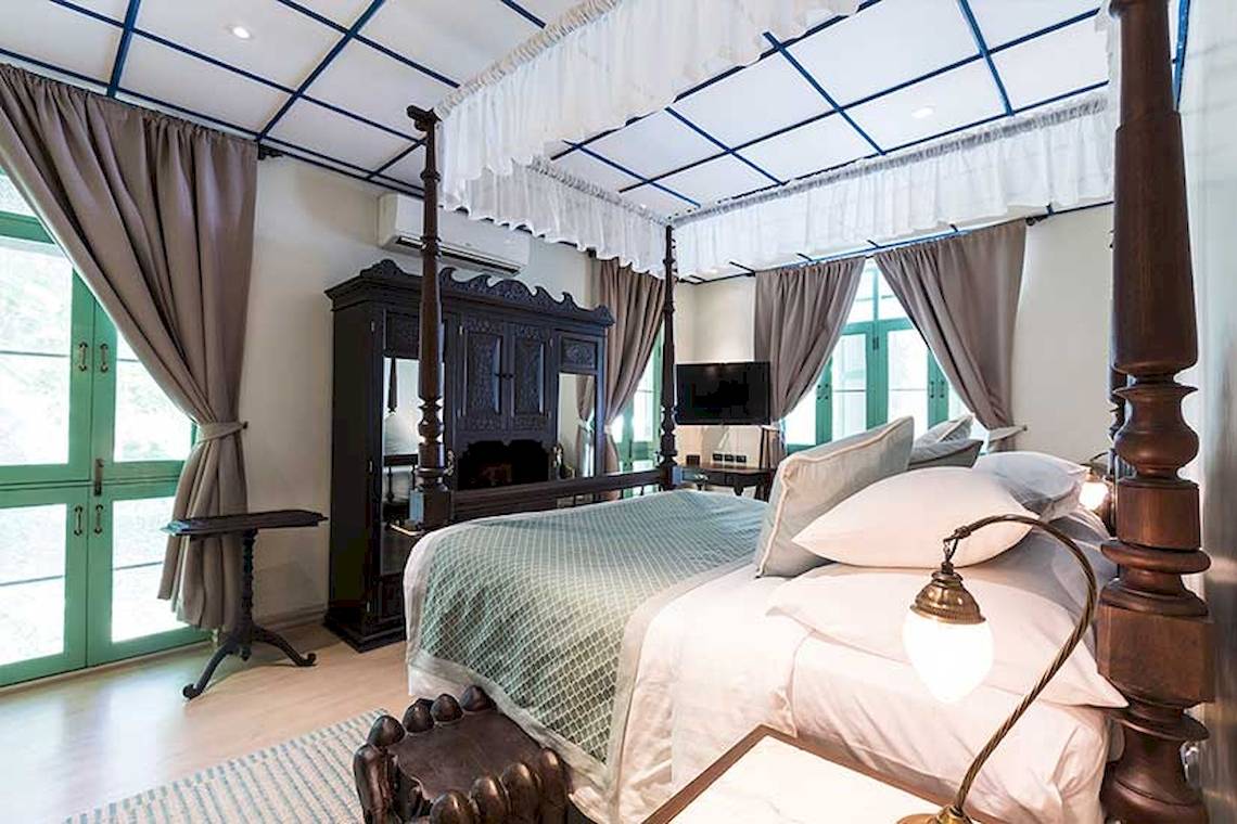 Schlafzimmer im Cape Panwa Hotel mit viersäuligem Bett, Vorhängen und Fernseher.