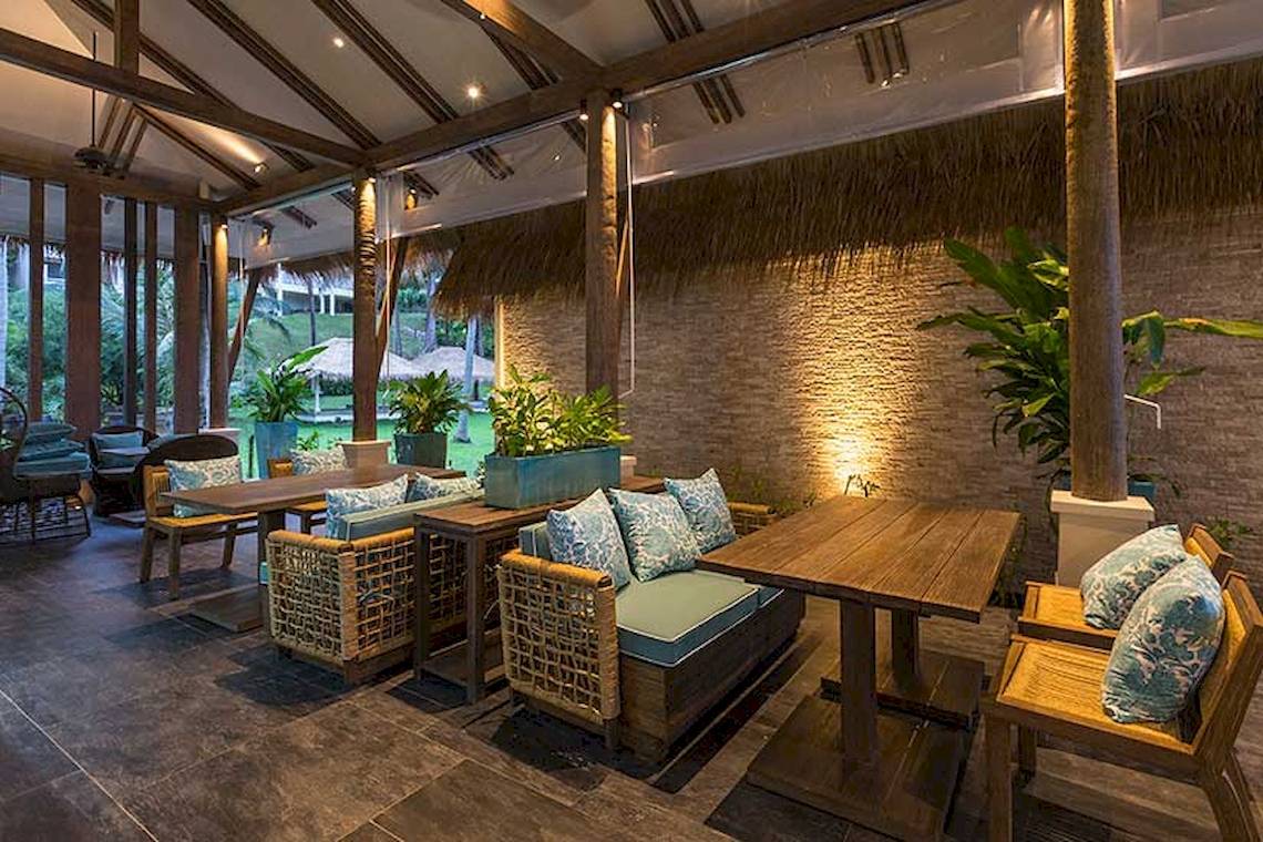 Innenbereich des Cape Panwa Hotels mit Holztischen, Stühlen und Pflanzen.