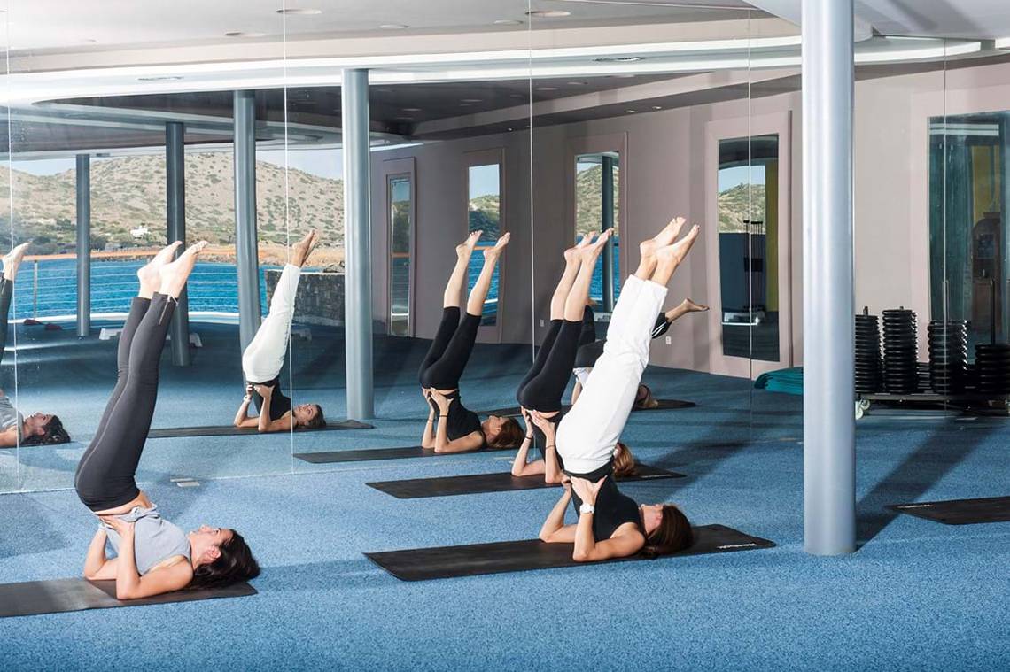 Frauen führen Yoga-Übungen im Elounda Bay Palace Hotel durch, die sich in Spiegeln spiegeln.