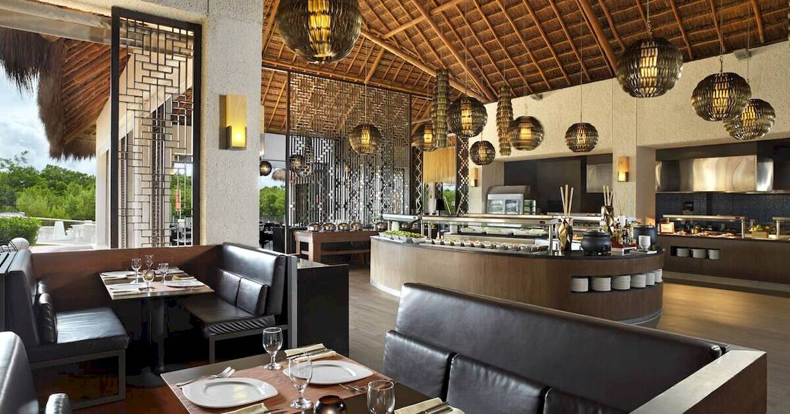 Innenraum des Paradisus Playa del Carmen Hotels mit modernem Design, schwarzen Ledersofas und einer Theke mit Essensangeboten.