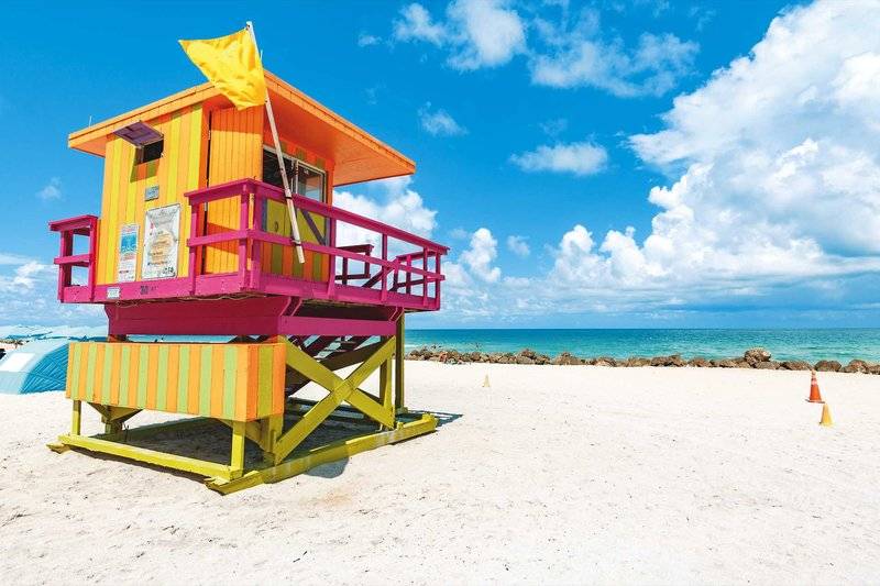 Eine bunte Rettungsstation steht auf einem weißen Sandstrand mit Blick auf das Meer.
