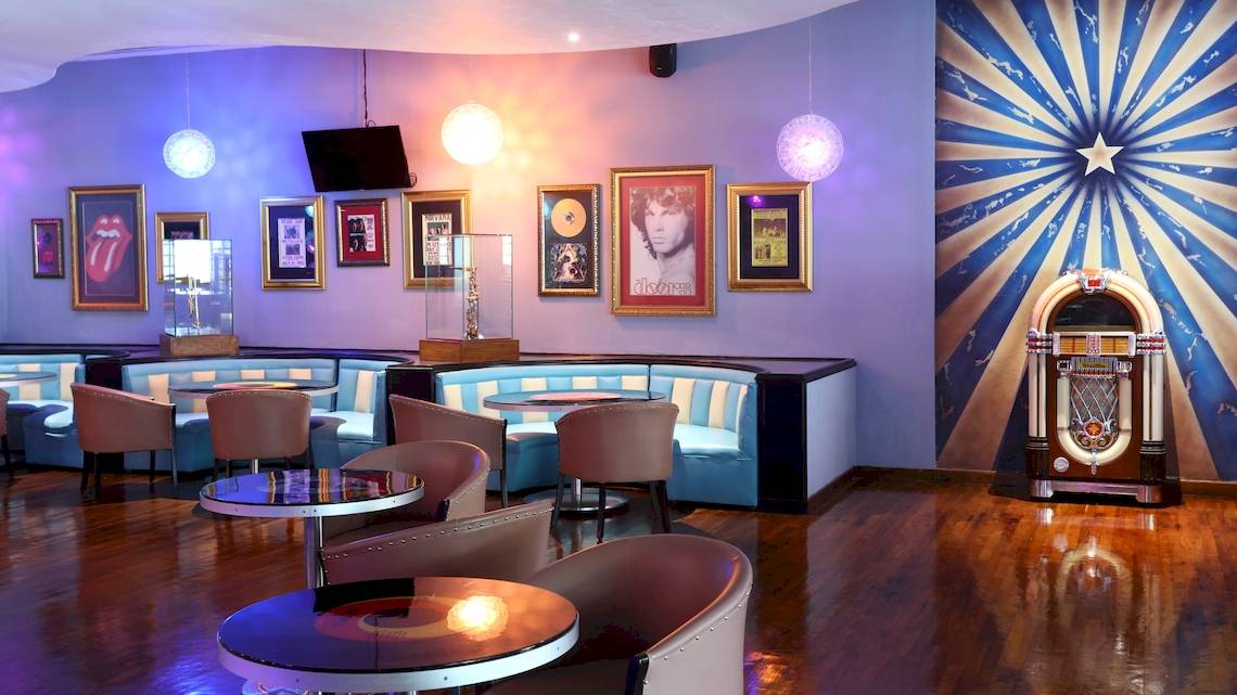 Innenansicht der Lobby im Iberostar Paraiso del Mar Hotel mit bunten Wänden, Jukebox und gerahmten Porträts.