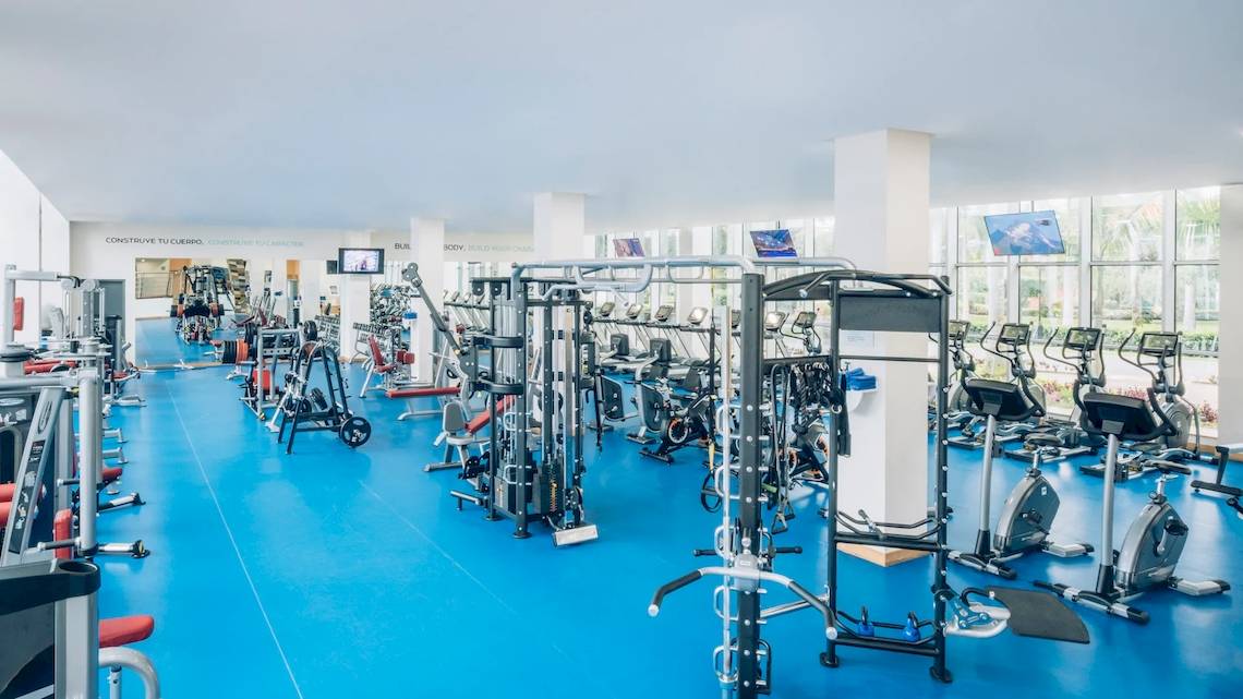 Fitnessstudio im Iberostar Paraiso del Mar Hotel mit vielen Geräten und blauen Böden.