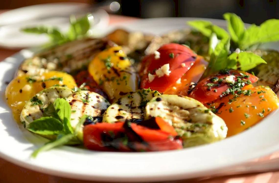 Ein Teller mit gegrilltem Gemüse, Tomaten und Basilikumblättern.